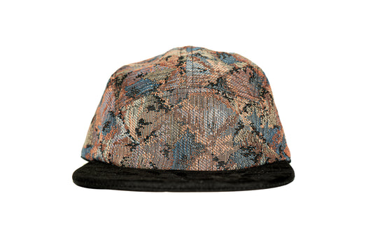 A structured five-panel cap featuring a textured, woven geometric pattern in shades of blue, orange, beige, and black, with a solid black flat brim.
