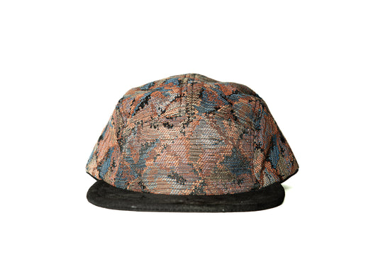 A structured baseball cap featuring a textured, multi-colored snakeskin pattern in shades of brown, orange, and blue, with a solid black flat brim, shown against a plain white background.